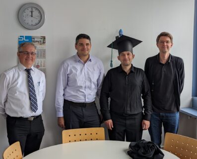 Auf dem Foto sind von links nach rechts Prof. Lenz, Prof. Blanas, Adnan Alhomssi und Prof. Leis nach der Promotionsprüfung zu sehen. Adnan Alhomssi trägt einen Doktorhut und lächelt in die Kamera.