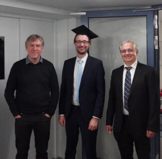 Auf dem Foto sind Prof. Lenz, Andreas Maximilian Wahl und Prof. Kapitza nach der Promotionsprüfung zu sehen. Alle drei Männer stehen nebeneinander. Andreas Maximilian Wahl ist in der Mitte und hat einen Doktorhut auf. Alle drei lächeln in die Kamera.